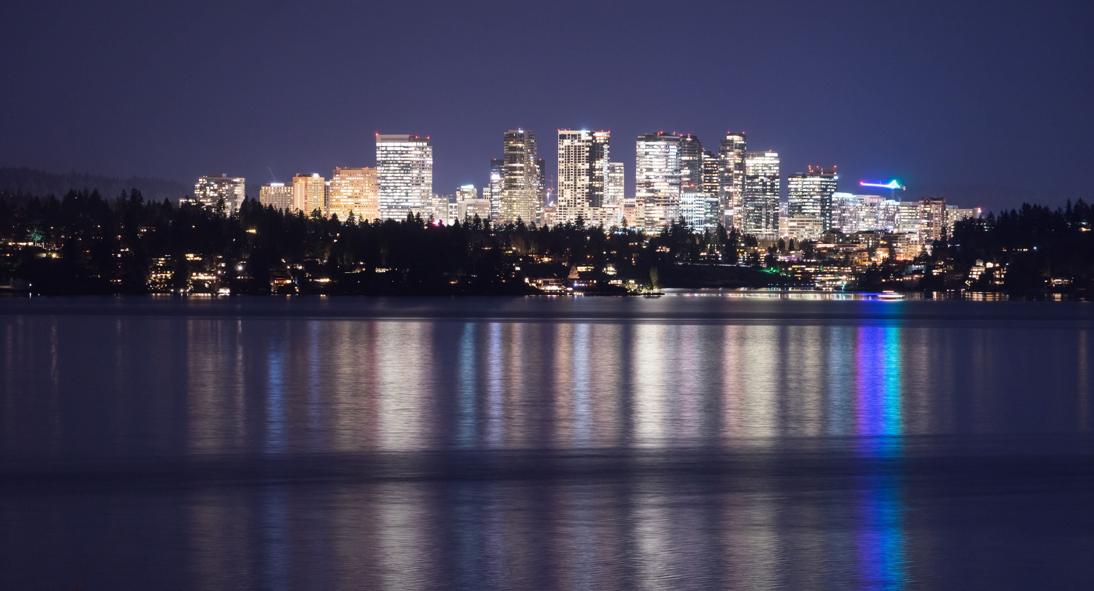 A city skyline at night with reflections on a body of water.