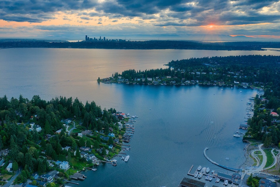 A coastal town with a marina, surrounded by dense forests and a large body of water.