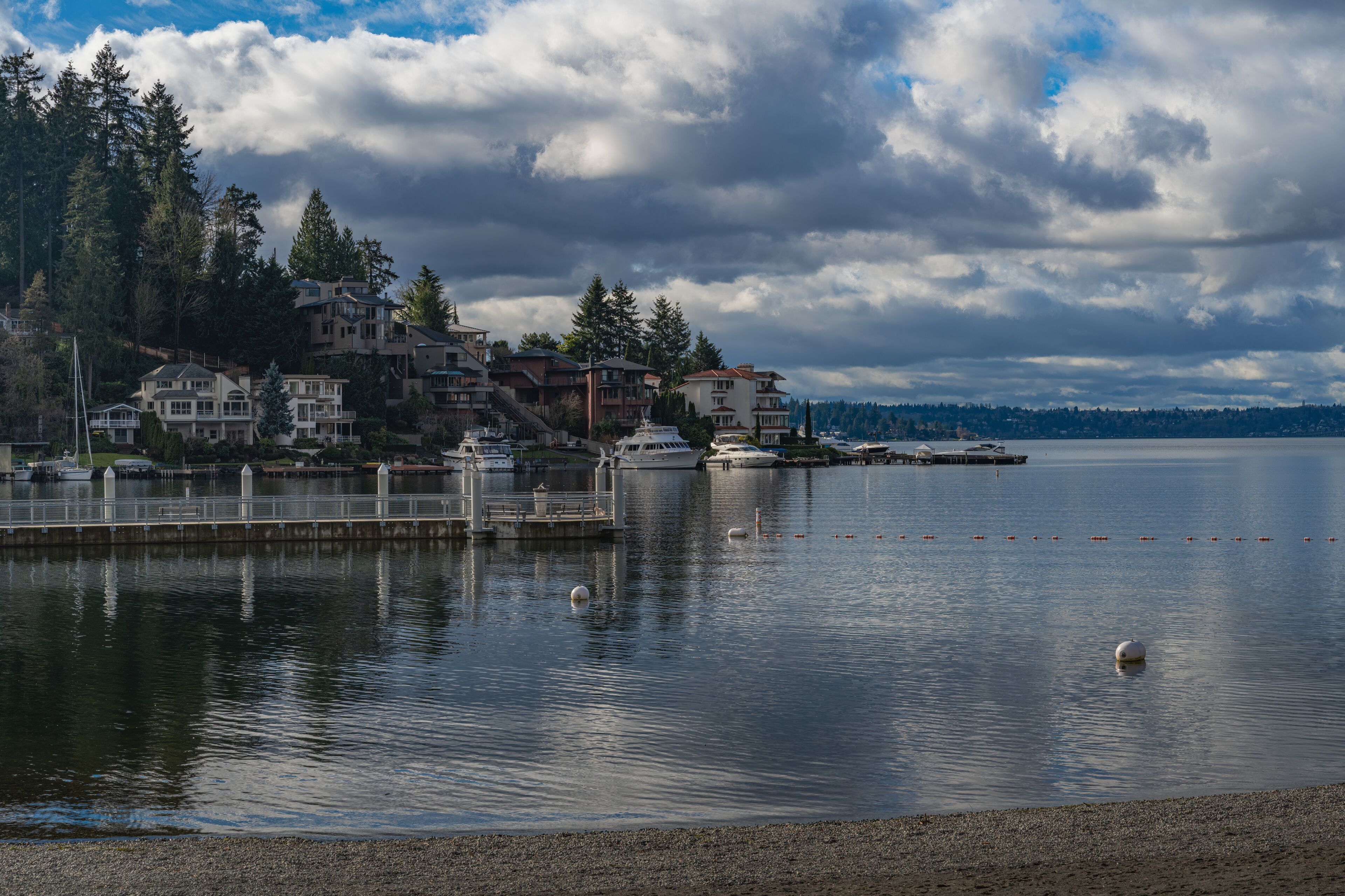 A calm waterfront with residential buildings, a dock, and a clear view of the distant shoreline.