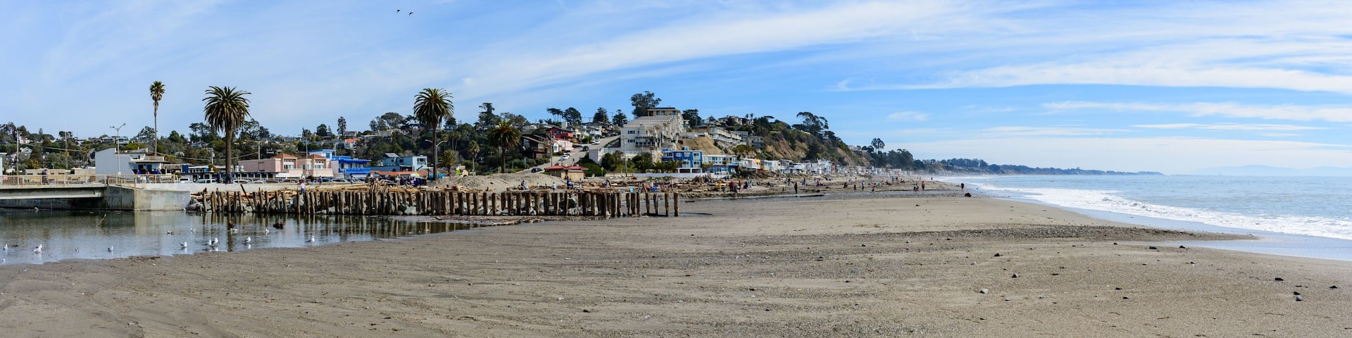 Scenic panoramic view of Rio Del Mar Beach near Santa Cruz California with a wooden pier stretching into water, flanked by coastal buildings and palms