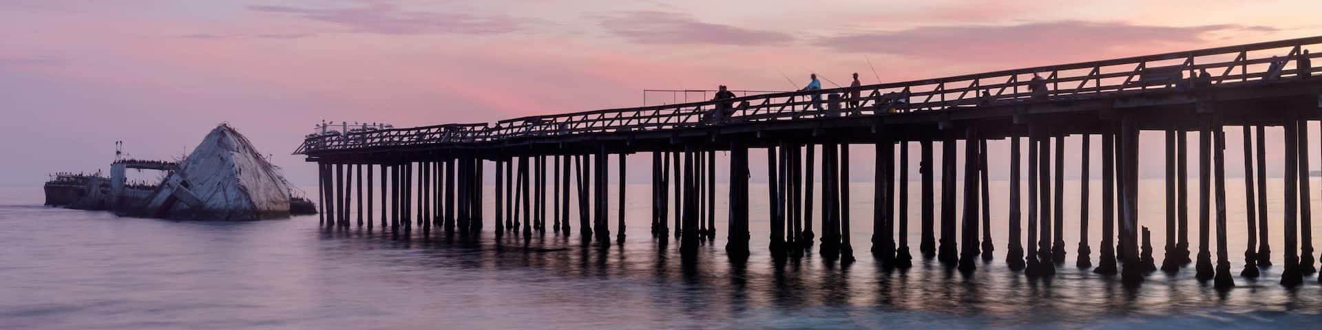 A pier extending into calm waters with a sunset sky.