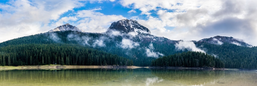 Montenegro, XXL panorama of durmitor mountains and black lake water surrounded by green coniferous forest in national park near zabljak