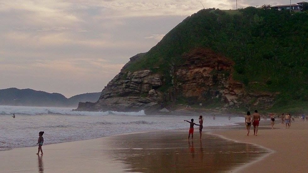 Une plage avec des vagues, des gens et une falaise.
