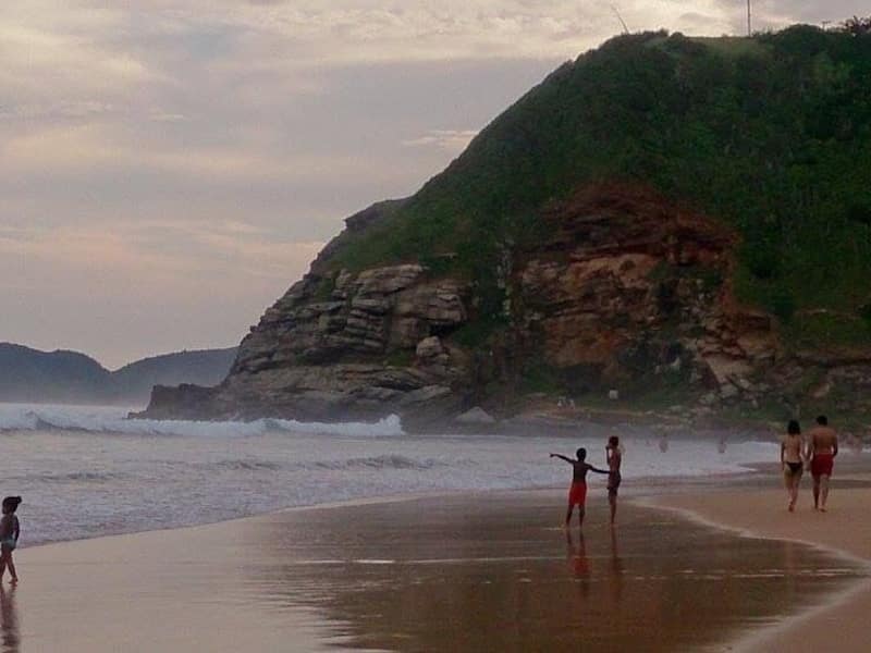A beach with waves, people, and a cliff.