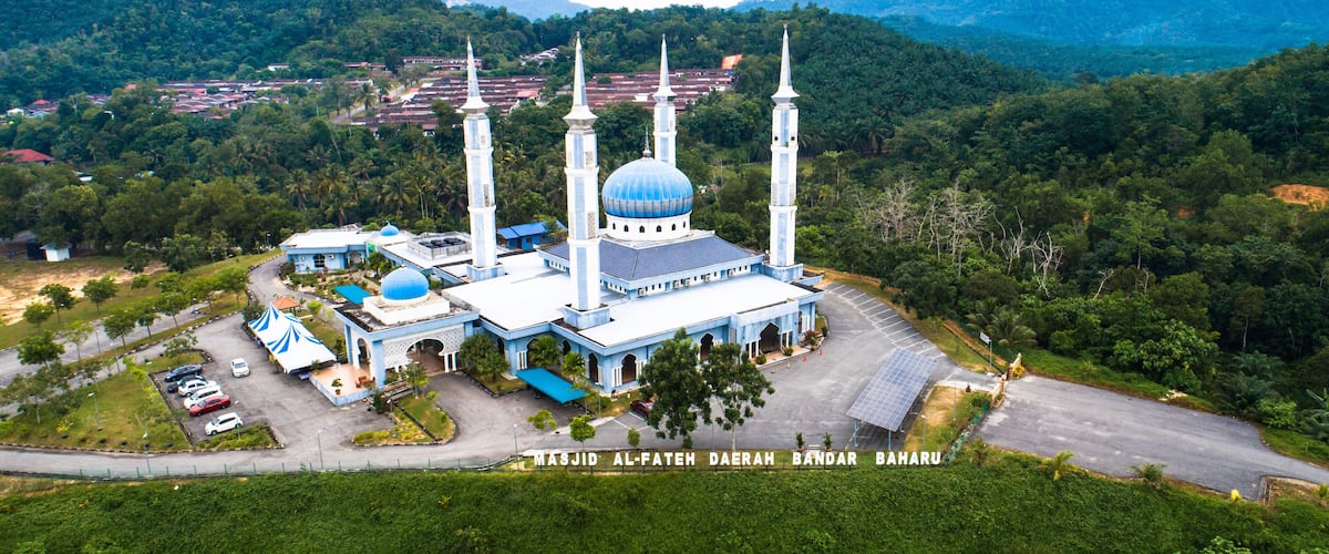 A mosque with a large dome and minarets, surrounded by lush greenery and hills.
