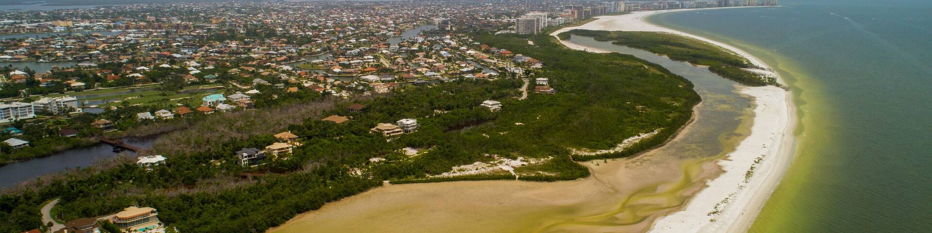 A coastal city with a long sandy beach, a river running parallel to the shore, and a dense urban area in the background.