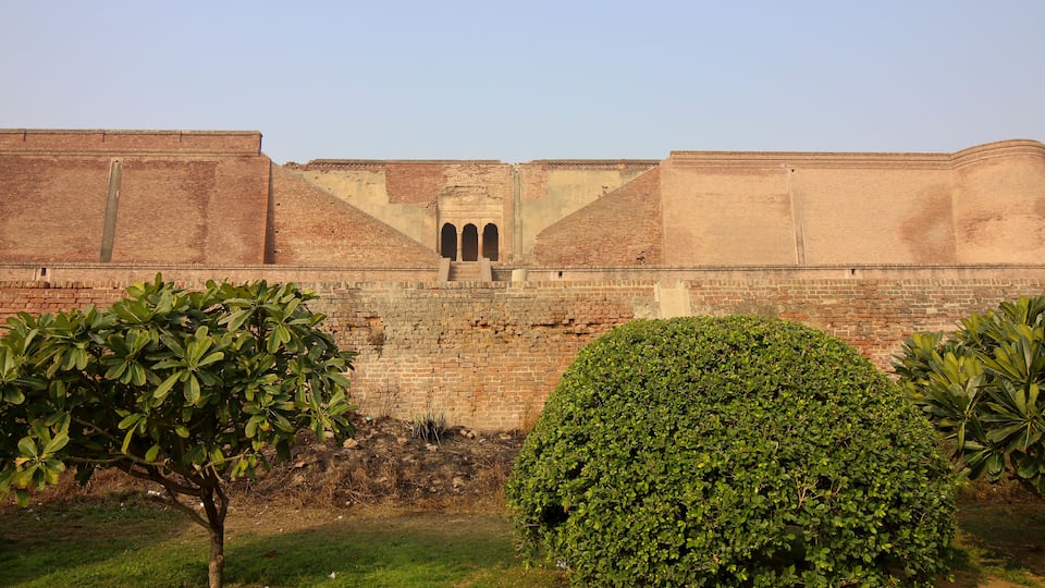 A brick fort with arched gateways and a well-maintained garden with trees and shrubs.