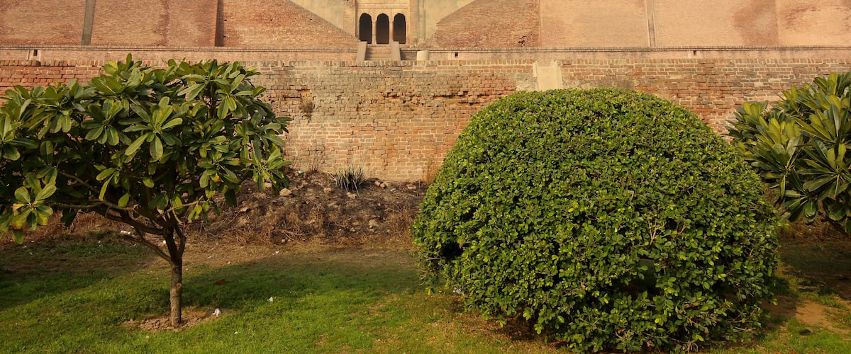 A brick fort with arched gateways and a well-maintained garden with trees and shrubs.