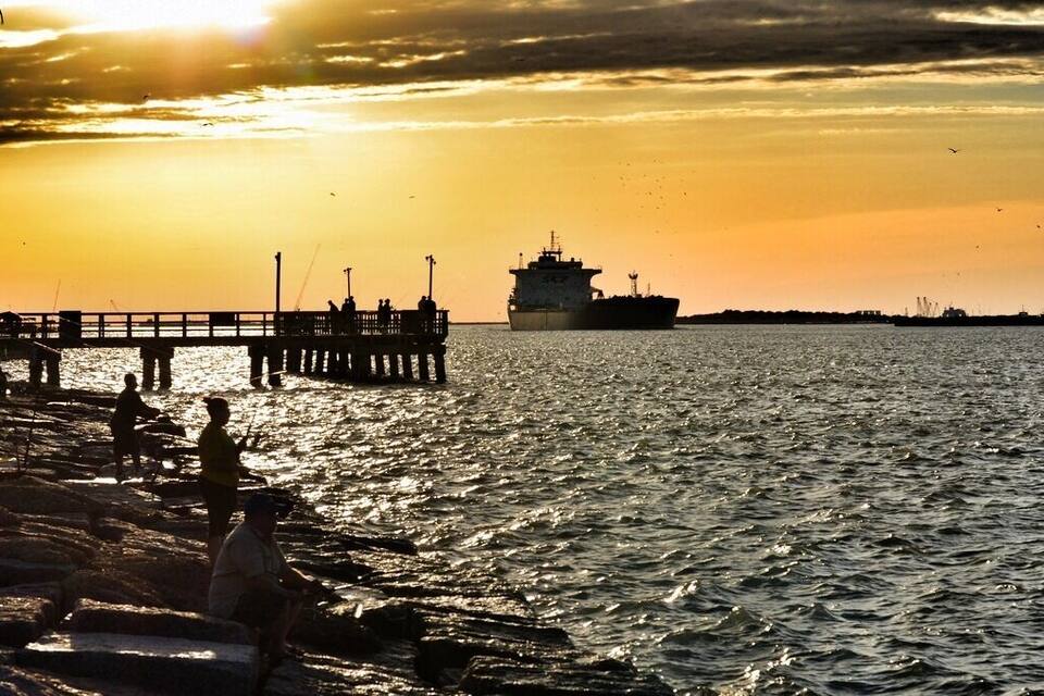 A sunset over a body of water with a pier and a large ship in the distance.