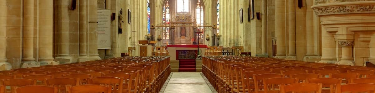 L’intérieur d’une cathédrale, avec de hauts plafonds en voûte, des rangées de bancs en bois et une allée centrale menant à l’autel.