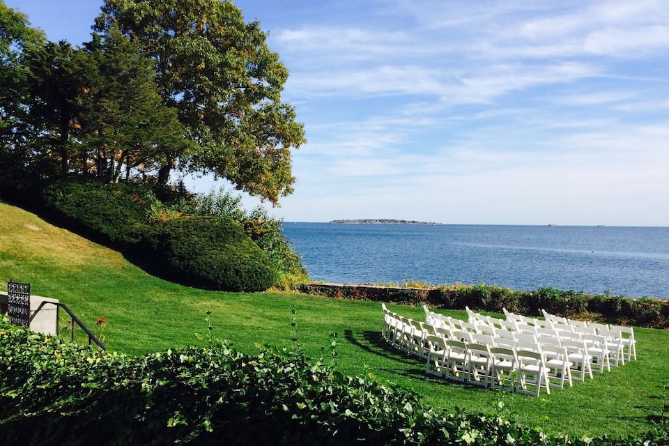 A grassy outdoor area with white chairs arranged in a semi-circle, overlooking a body of water.