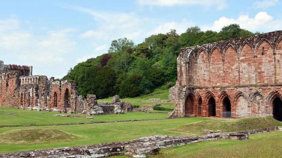 Ancient ruins with arched doorways and a grassy field.