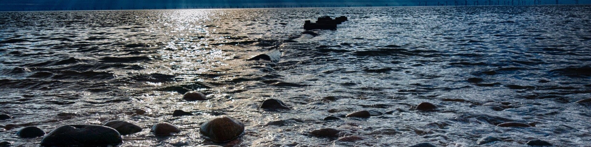 Una costa rocosa con cielo nublado y reflejos de sol en el agua.