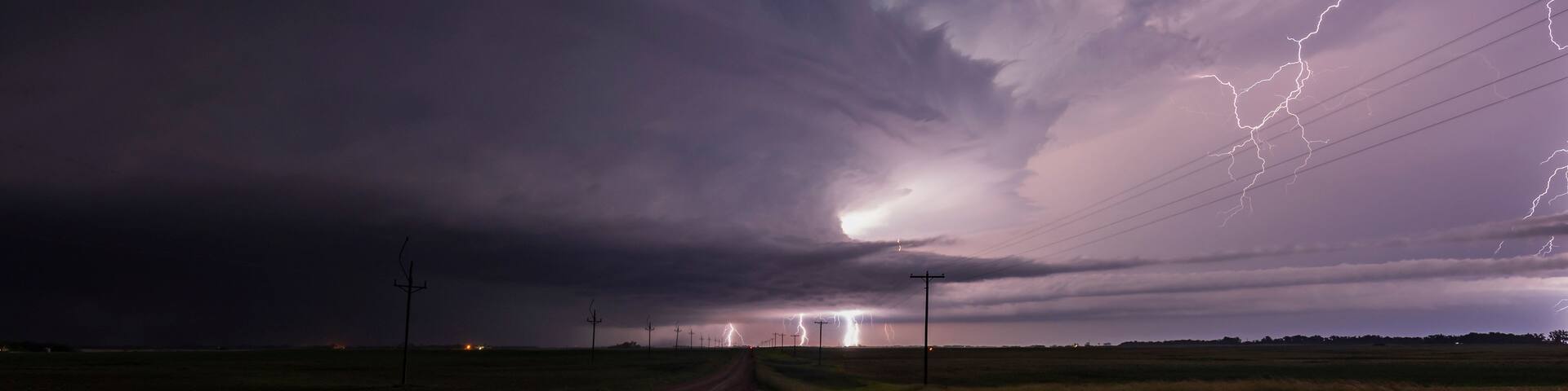 A rural landscape with a dirt road leading to a distant city, under a stormy sky with lightning.