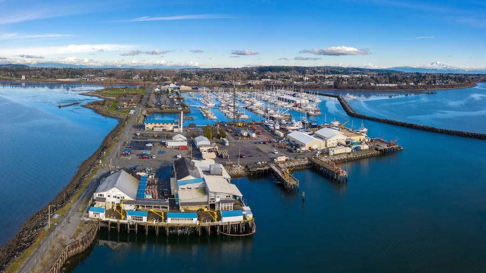 An aerial view of a harbor with boats, a dock, and a mountainous backdrop.