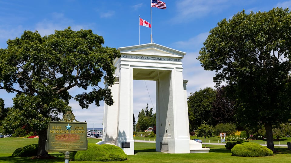 A white monument with flags, surrounded by trees and a sign for Blue Star Memorial Highway.