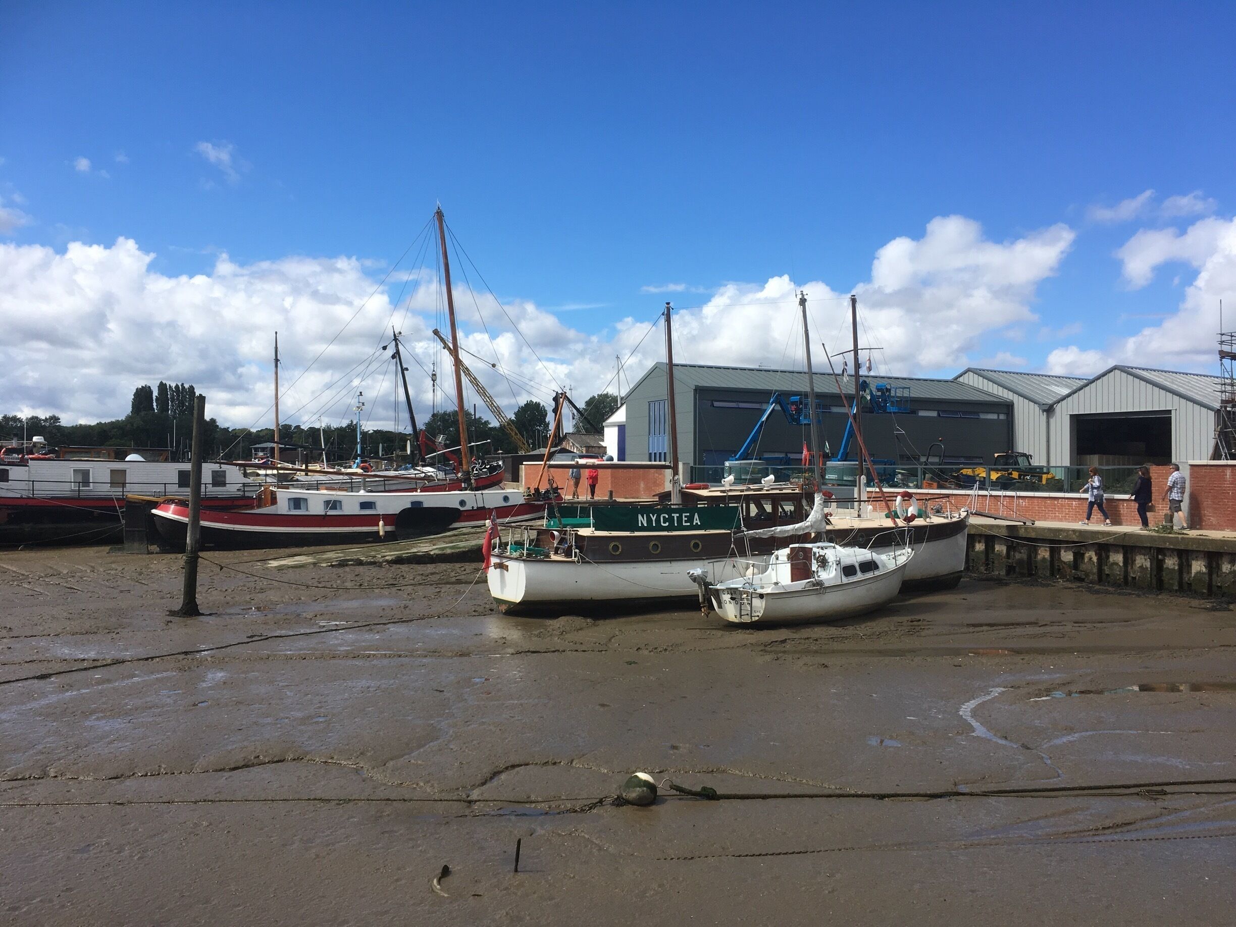 A harbor with several boats docked, a large industrial building, and a clear blue sky.