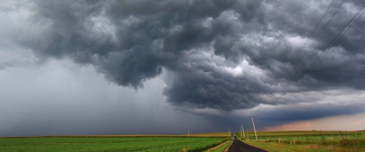 A rural landscape with a road, green fields, and a stormy sky.