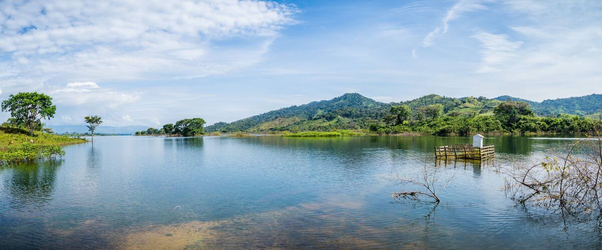 A calm lake with a wooden dock, surrounded by lush greenery and hills.