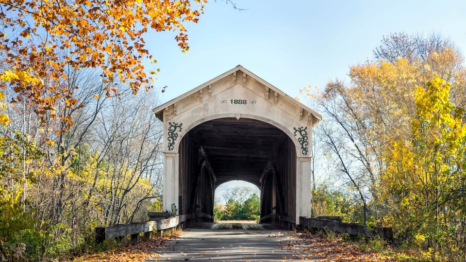A covered bridge with the year 1888 marked on it, surrounded by autumn foliage.