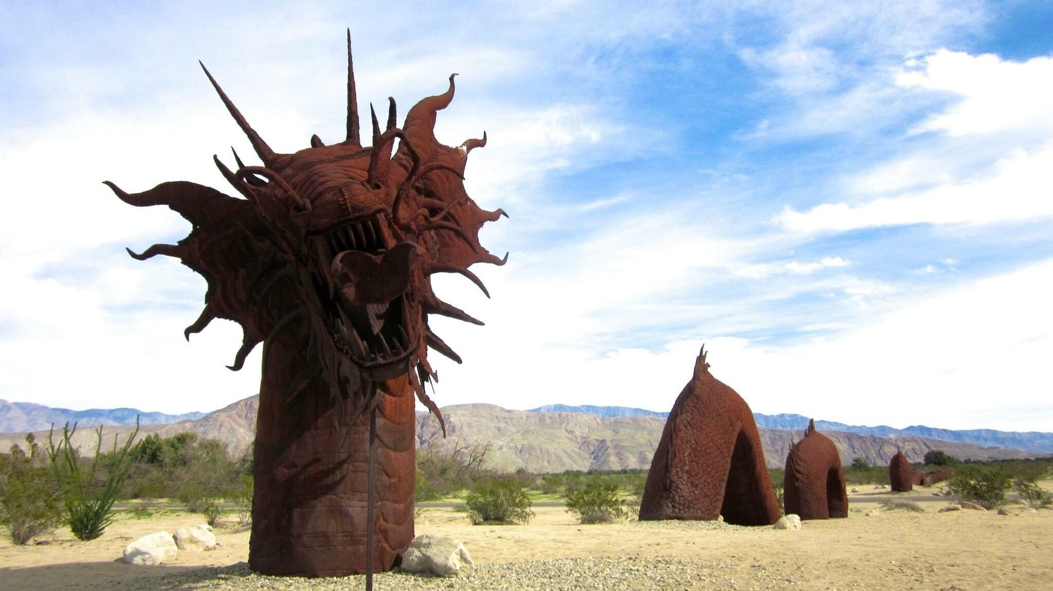 A desert landscape with large rock formations resembling a dragon and other similar structures.