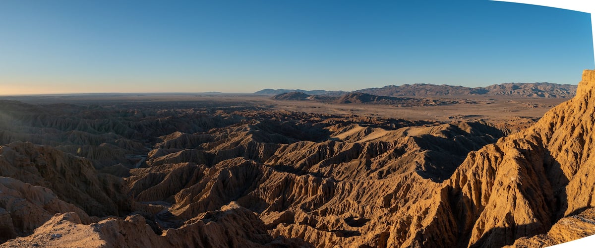 A vast desert landscape with rugged terrain and distant mountains under a clear sky.