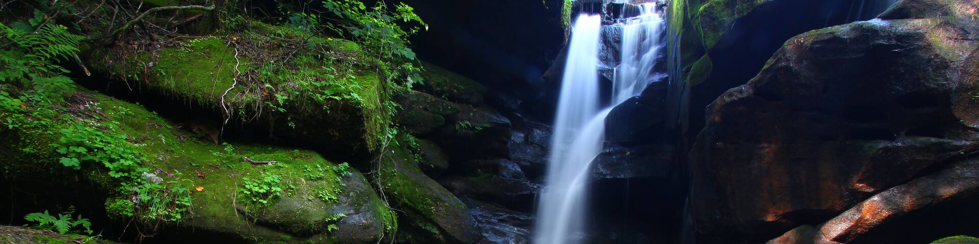 A waterfall cascading over moss-covered rocks in a forested area.