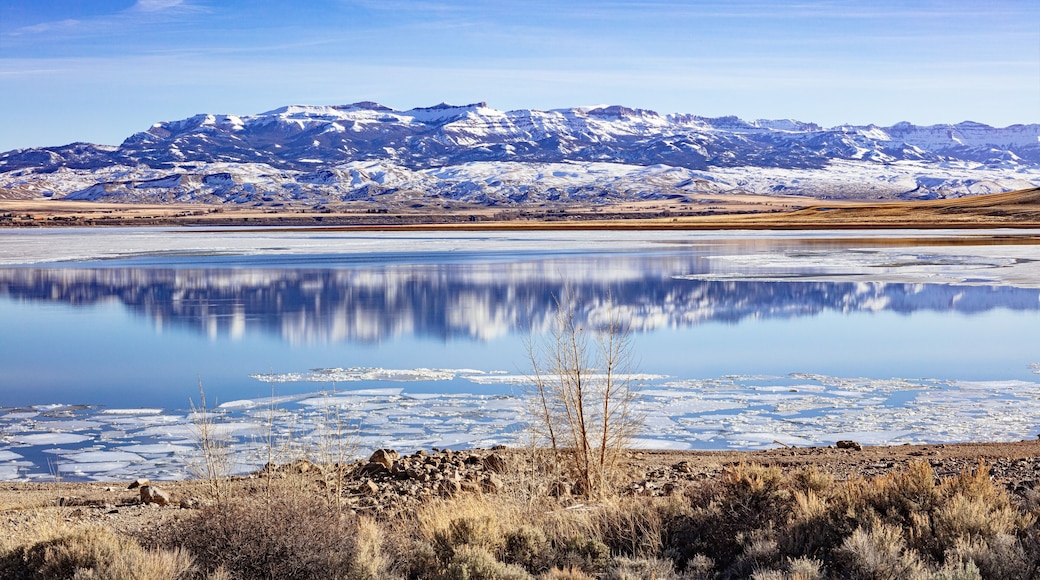 Buffalo Bill Cody Reservoir and snow-covered Carter Mountain Range during spring with ice in the water and blue cloudy sky during spring in Wyoming, USA.
