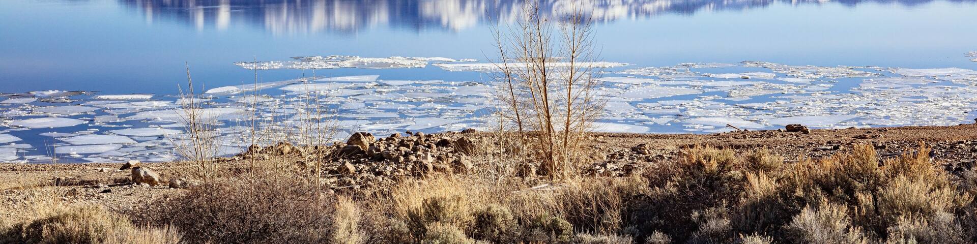 Buffalo Bill Cody Reservoir and snow-covered Carter Mountain Range during spring with ice in the water and blue cloudy sky during spring in Wyoming, USA.
