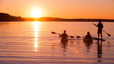 kayakers and stand up paddle boarder on lake at sunset