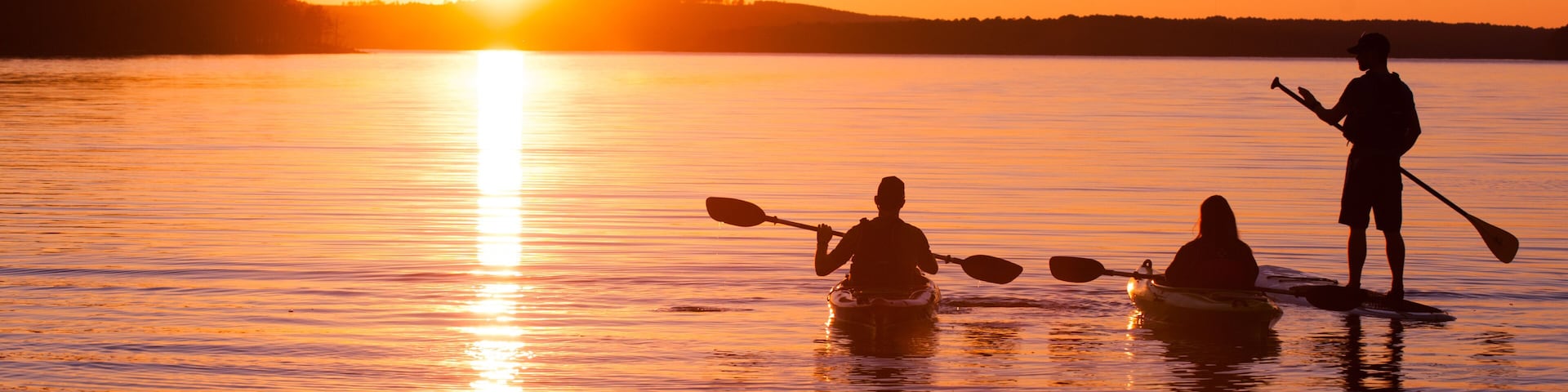 kayakers and stand up paddle boarder on lake at sunset