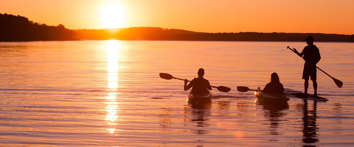 A sunset over a calm lake with kayakers.