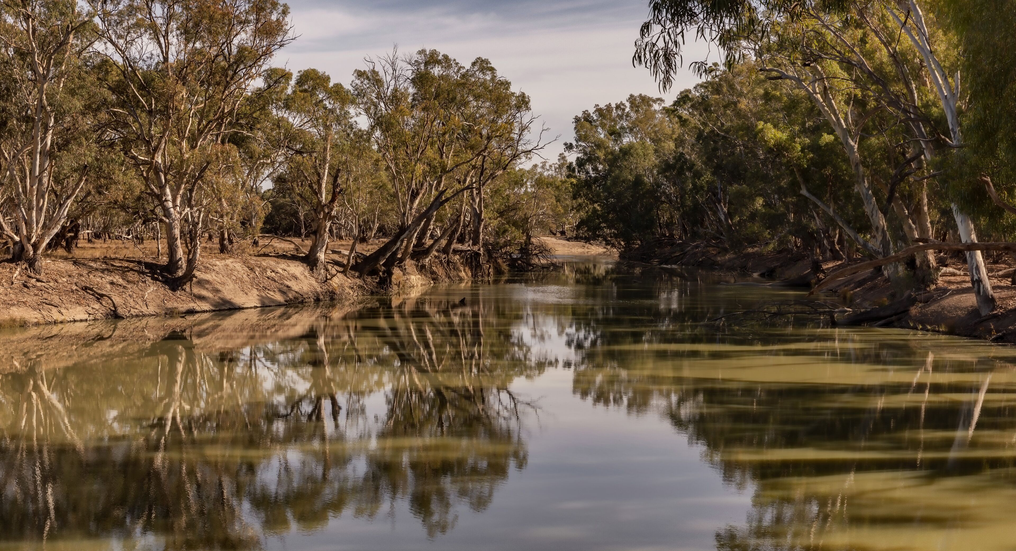 A calm river with reflections of trees and a clear sky.