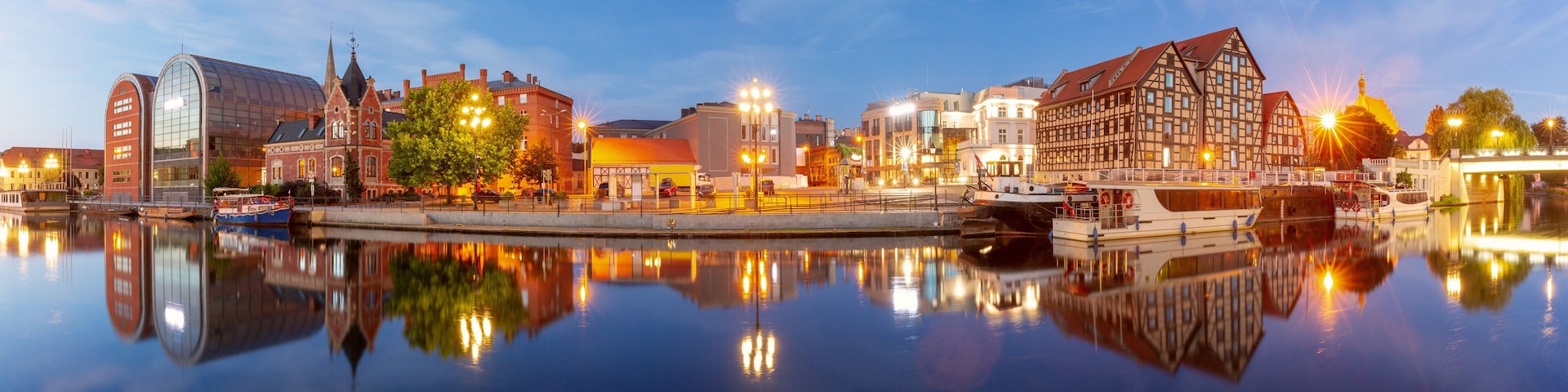 Panoramic view of Bydgoszcz waterfront at dusk, showing historic and modern buildings along the Brda River in Poland