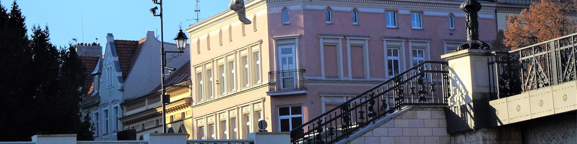 A statue of a man balancing on a tightrope with a bird on his head, set against a backdrop of historic buildings and a clear blue sky.