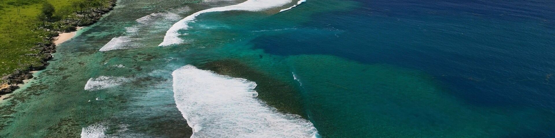 Un paisaje costero con aguas turquesas cristalinas, una playa de arena y vegetación verde.