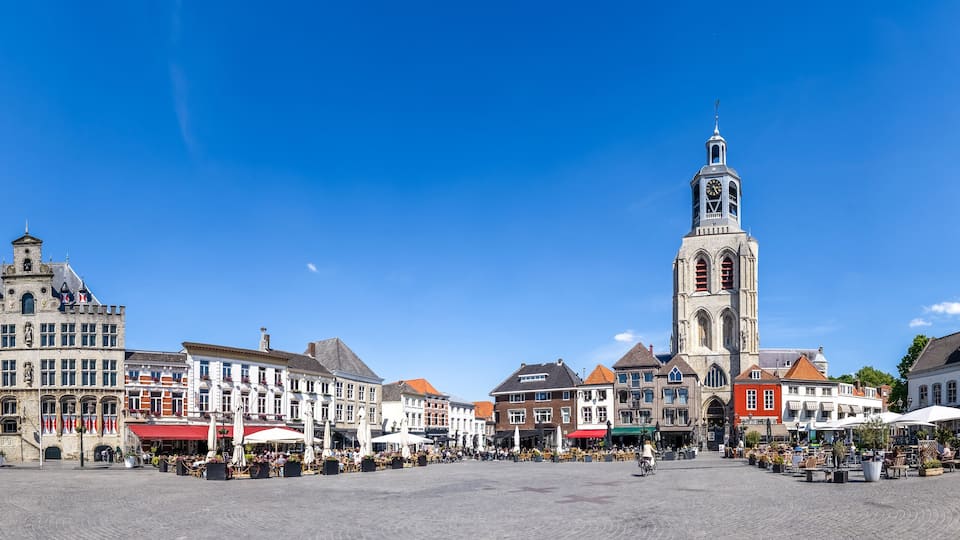 A historic square with a prominent clock tower, surrounded by traditional European architecture and outdoor cafes.