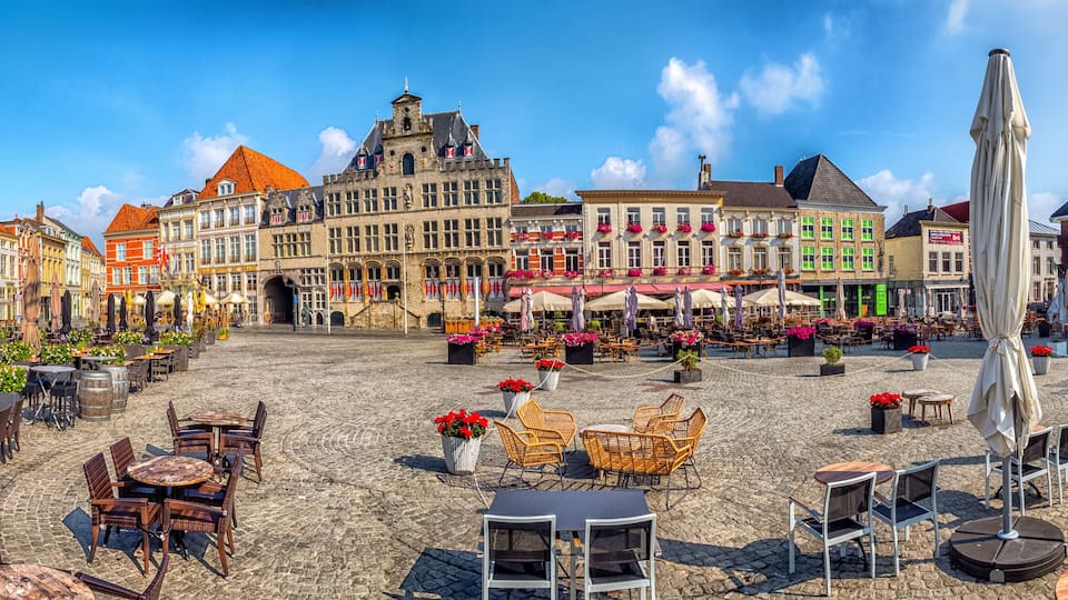 A cobblestone square with outdoor seating, historic buildings, and a church tower.