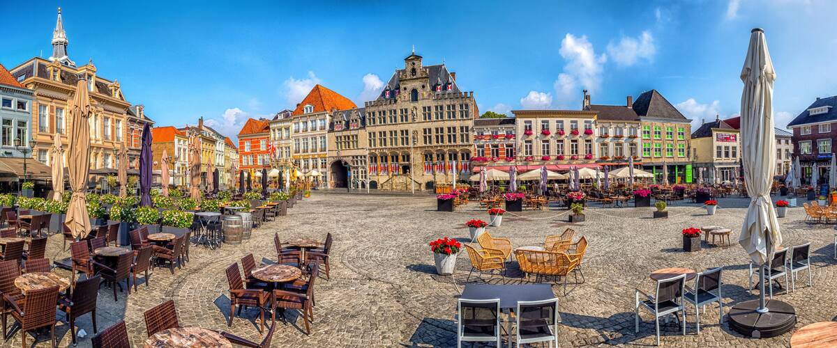 A cobblestone square with outdoor seating, historic buildings, and a church tower.