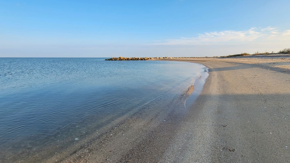 A calm beach with clear water, a sandy shore, and a rocky outcrop in the distance.