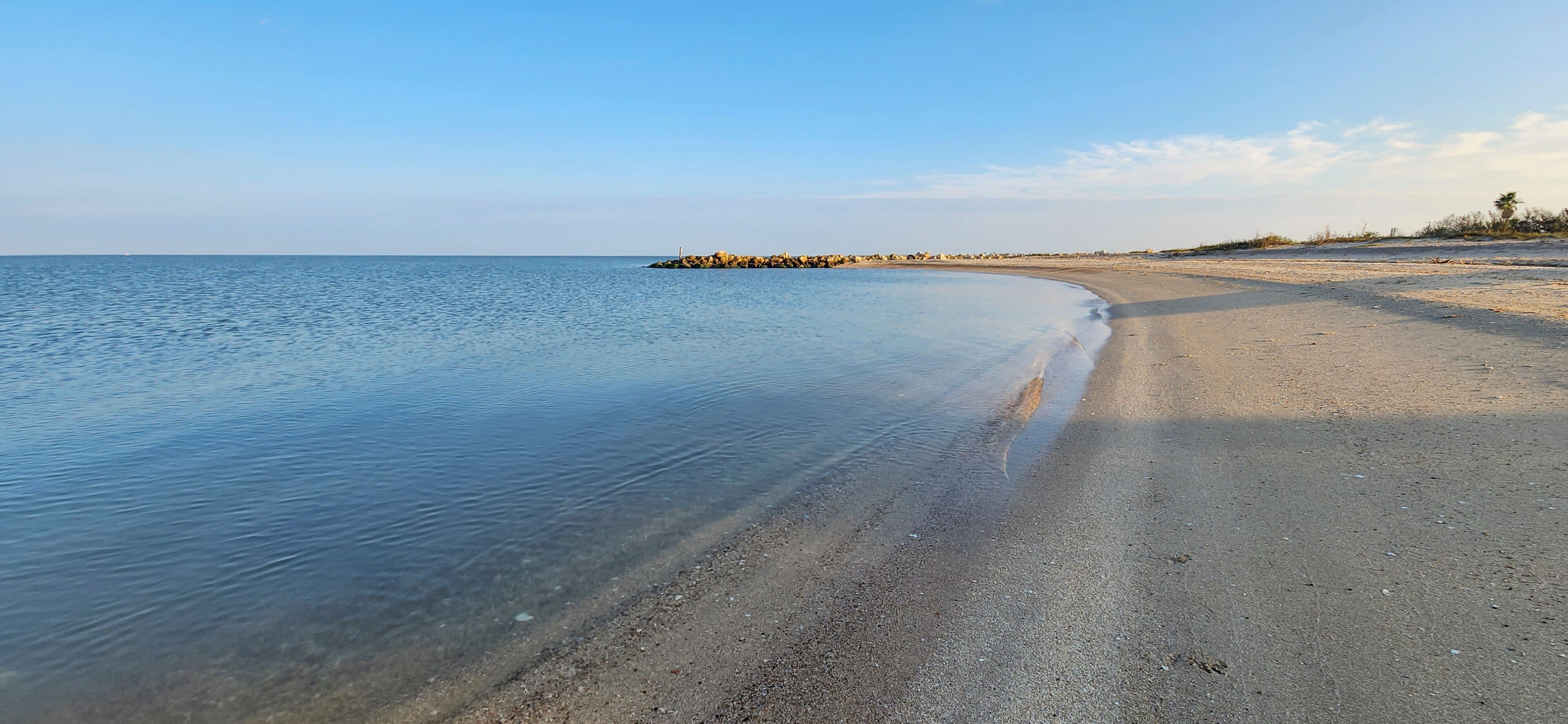 A calm beach with clear water, a sandy shore, and a rocky outcrop in the distance.