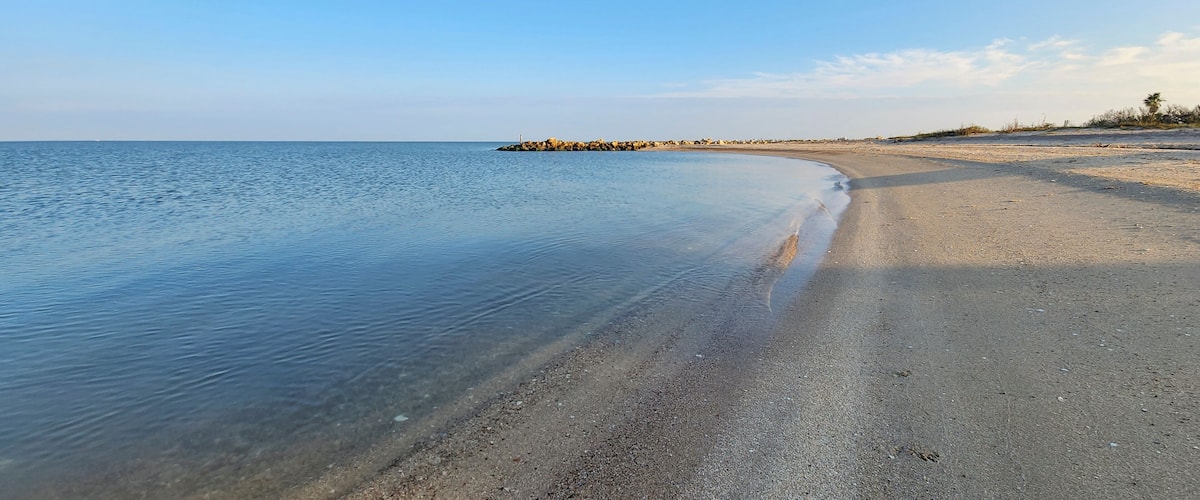 A calm beach with clear water, a sandy shore, and a rocky outcrop in the distance.