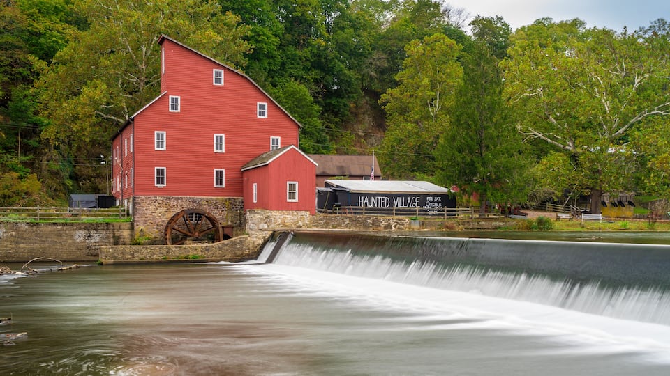 A red mill with a water wheel, surrounded by lush greenery and a small building labeled "Haunted Village".