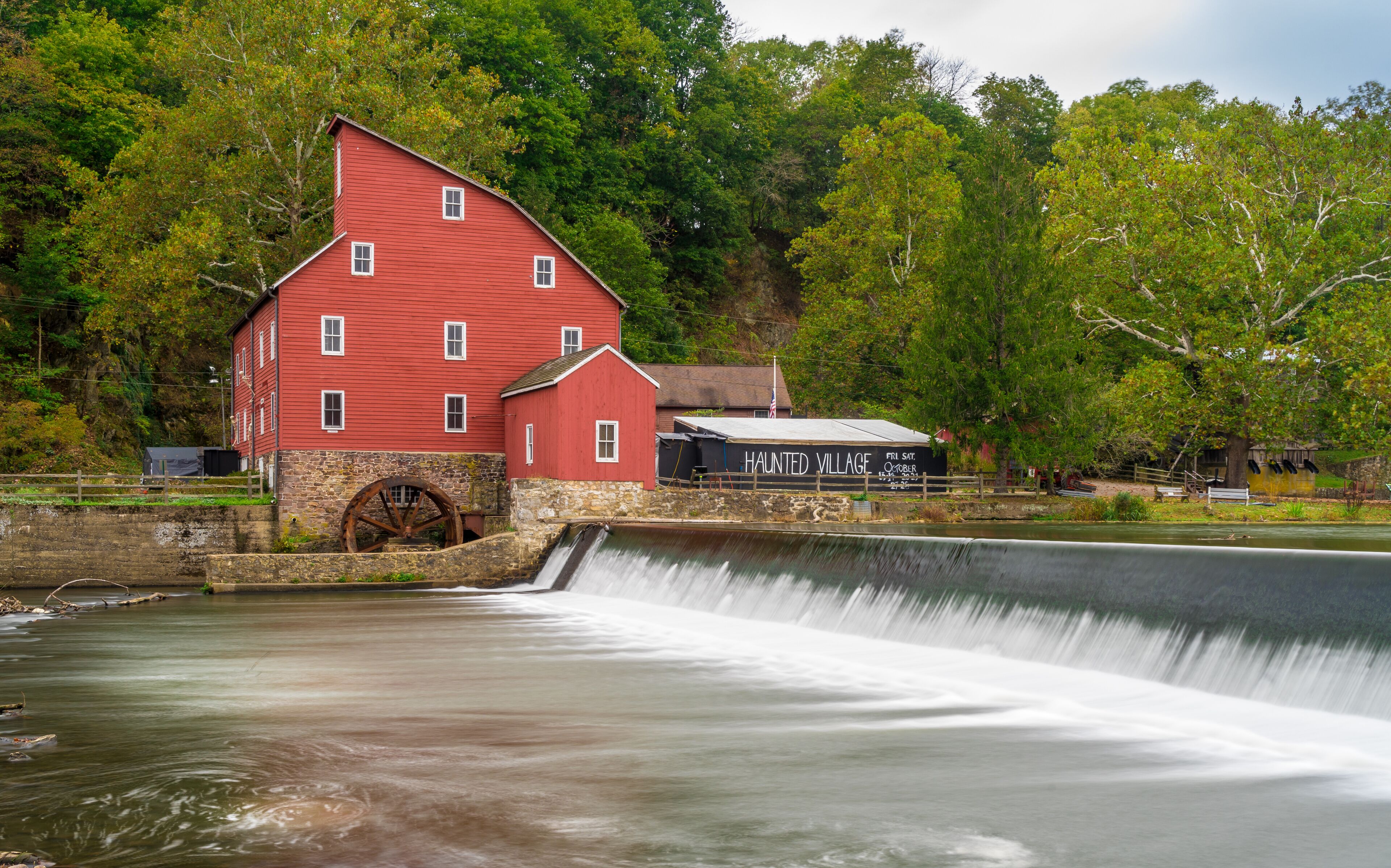 A red mill with a water wheel, surrounded by lush greenery and a small building labeled "Haunted Village".