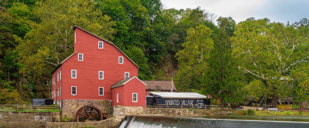 A red mill with a water wheel, surrounded by lush greenery and a small building labeled "Haunted Village".
