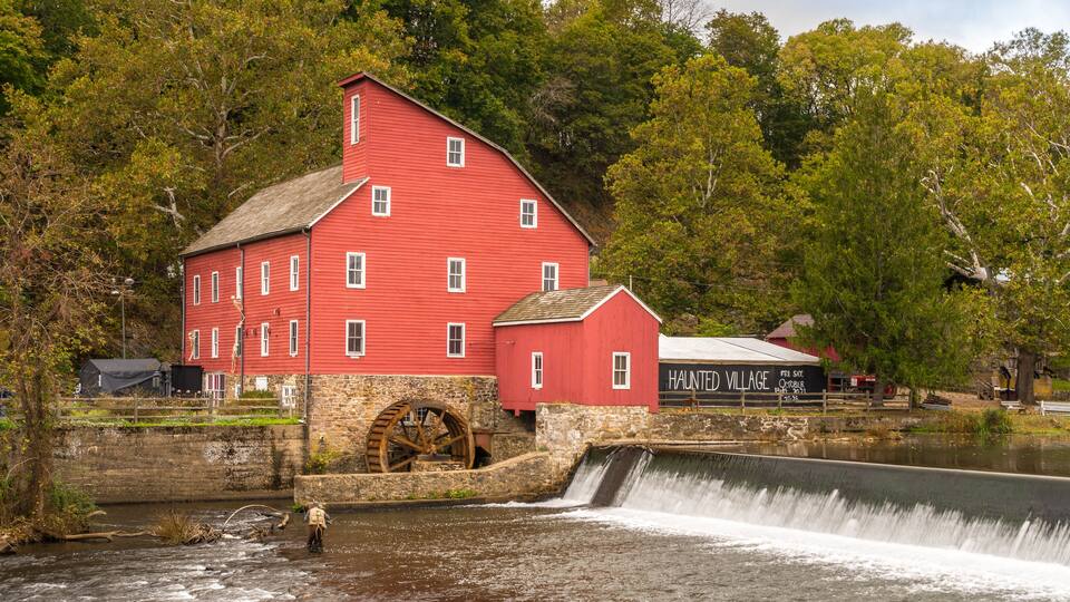 A red mill with a water wheel and a sign for 'Haunted Village'.