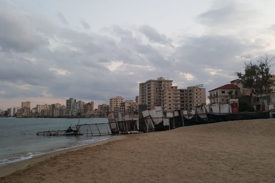 A beach with a metal fence and buildings in the background.