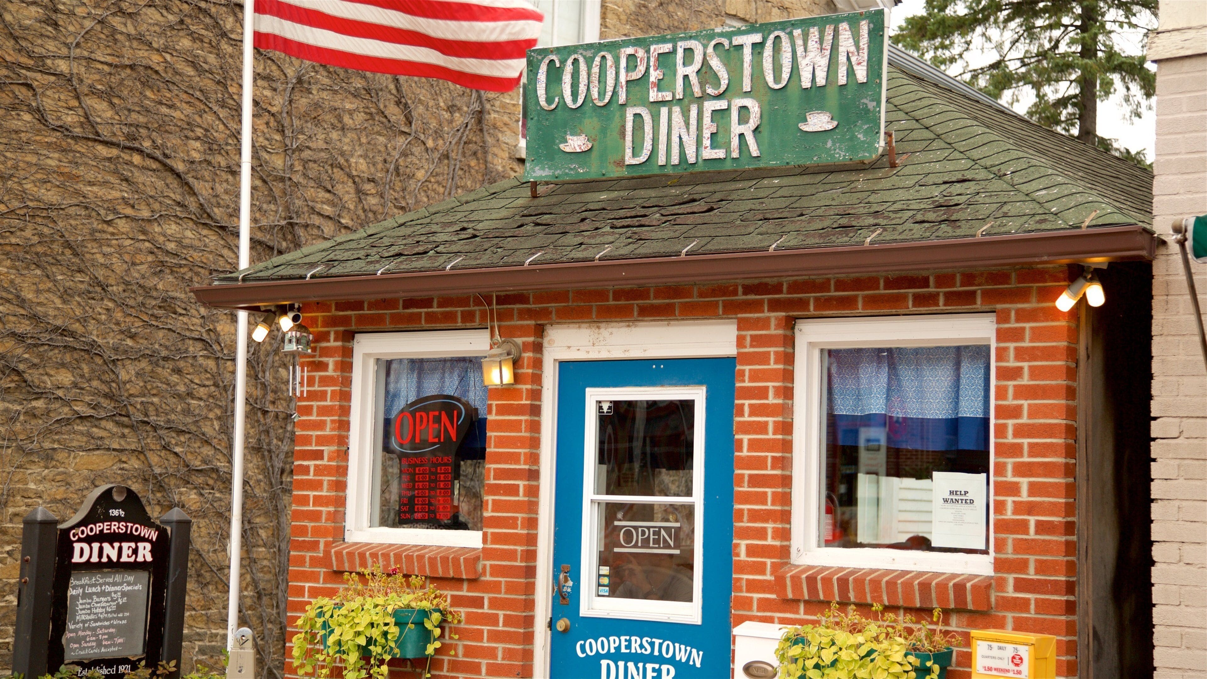 A brick diner with a blue door and windows, a sign reading "Cooperstown Diner," and a flagpole with an American flag.