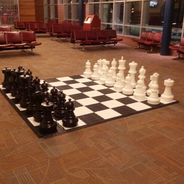 A large chessboard with pieces set up in an airport terminal.