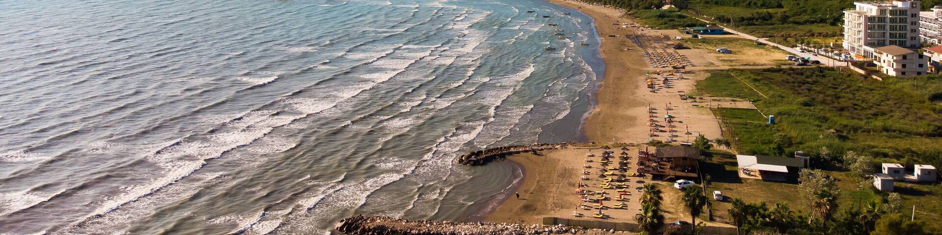 View to sandy beach of Adriatic Sea and to the city of Durres, Albania during sunset.